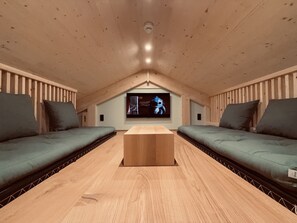 Un acogedor cuarto ático con techo de madera, dos sofás, una mesa de centro y una gran pantalla de televisión mostrando una película.