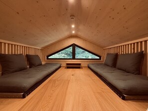 A room with a sloped ceiling, two sofas facing each other, a window with a view of greenery, and a wooden floor. - 03_NTH032_Deluxe Chalet mit Sauna und Hot Tub by Interhome (Großveitsch)