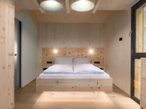 A wooden room with a bed, two wall-mounted lights, and a window. - 03_NTH032_Deluxe Chalet mit Sauna und Hot Tub by Interhome (Großveitsch)
