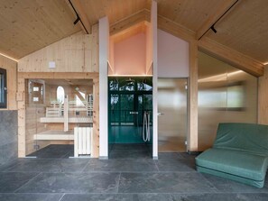 A modern interior with a wooden ceiling, a glass door leading to a shower area, and a green sofa. - 03_NTH032_Deluxe Chalet mit Sauna und Hot Tub by Interhome (Großveitsch)