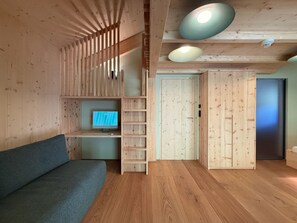 A room with a wooden floor, a grey sofa, a TV on a wooden shelf, and a door with a frosted glass panel. - 03_NTH032_Deluxe Chalet mit Sauna und Hot Tub by Interhome (Großveitsch)