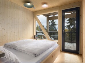 A bedroom with a bed, a window, and a view of trees. - 03_NTH032_Deluxe Chalet mit Sauna und Hot Tub by Interhome (Großveitsch)