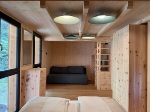 A wooden interior with a bed, a sofa, and built-in shelving. - 03_NTH032_Deluxe Chalet mit Sauna und Hot Tub by Interhome (Großveitsch)