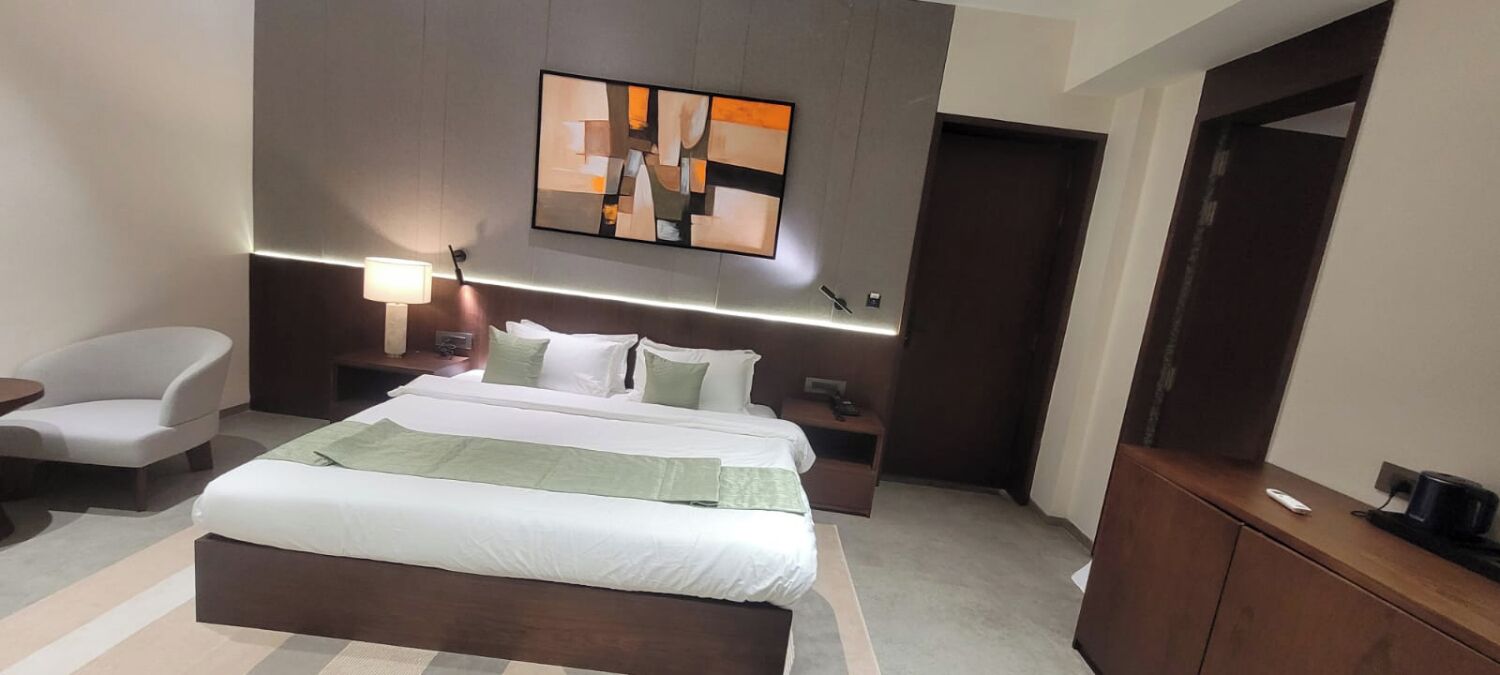 Una habitación de hotel moderna con una cama grande, una mesita de noche, una silla, un escritorio y un cuadro en la pared.