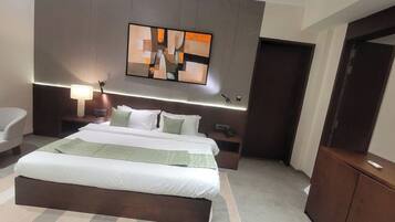 A modern hotel room with a large bed, a bedside table, a chair, a desk, and a painting on the wall.