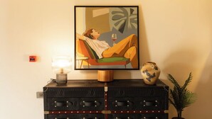 Une pièce avec un tableau encadré représentant une personne se relaxant, une table de chevet avec une lampe, un vase décoratif et un panneau indiquant la sortie de secours.