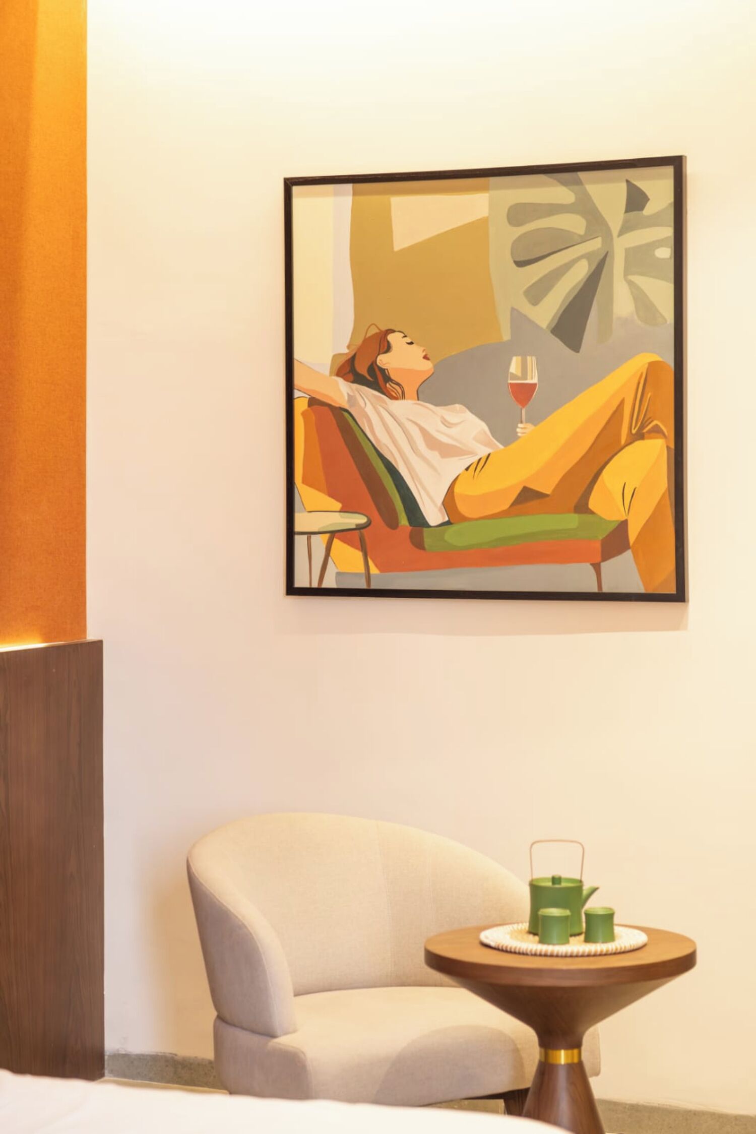 Hotellihuoneessa on sänky, tuoli, pieni pöytä, jossa on lasi ja vihreä astia, sekä seinällä taulu.