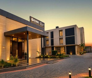 Un hôtel doté d’une architecture moderne, avec une enseigne bien visible indiquant « KIWA By Rustic Toys Hotel Restaurant Banquet ».
