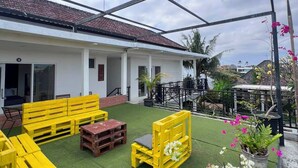An outdoor patio area with yellow furniture and artificial grass, a white building with a tiled roof, and potted plants. - private room with bigger size room, near central canggu,
10minute to the beach (badung)