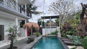 A swimming pool with a thatched roof structure, surrounded by potted plants and a modern building with a balcony. - private room with bigger size room, near central canggu,
10minute to the beach (badung)