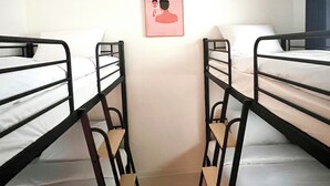 Et soveværelse med køjesenge, en enkelt seng, en hængende lampe og et billede i ramme på væggen.