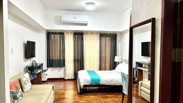 Una habitación de hotel con una cama, un sofá, un escritorio y un ventilador, y un televisor.