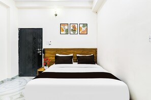 A bedroom with a bed, a wooden headboard, a black door, and three framed artworks on the wall.