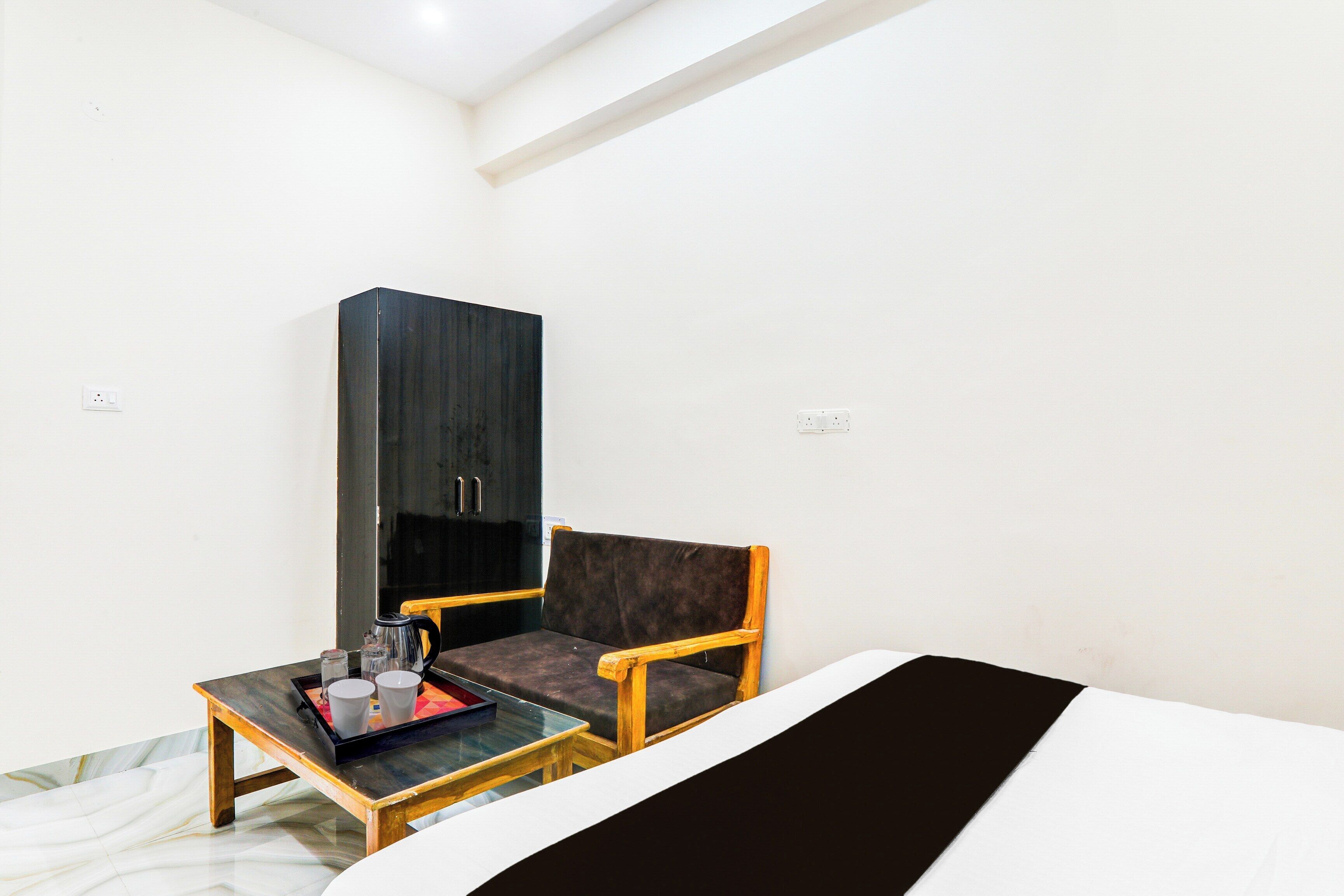 A small room with a bed, a wooden chair, a small table with a tray, and a dark-colored wardrobe.