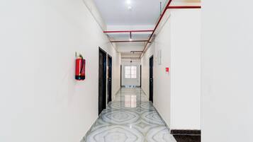 A corridor with a patterned floor, fire extinguishers, and a ceiling with visible pipes.