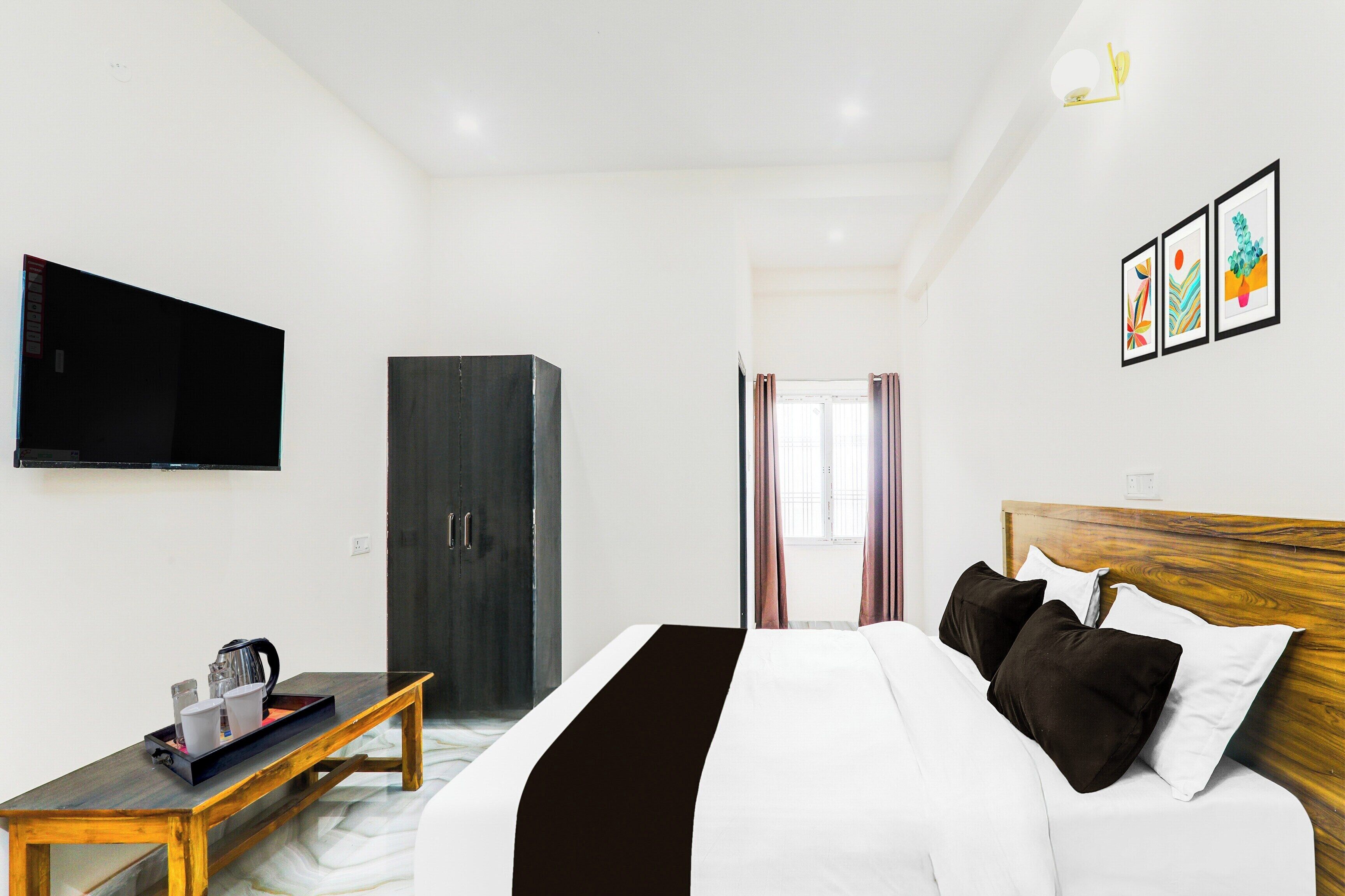 A hotel room with a bed, a television, a wardrobe, and a desk with a tray.