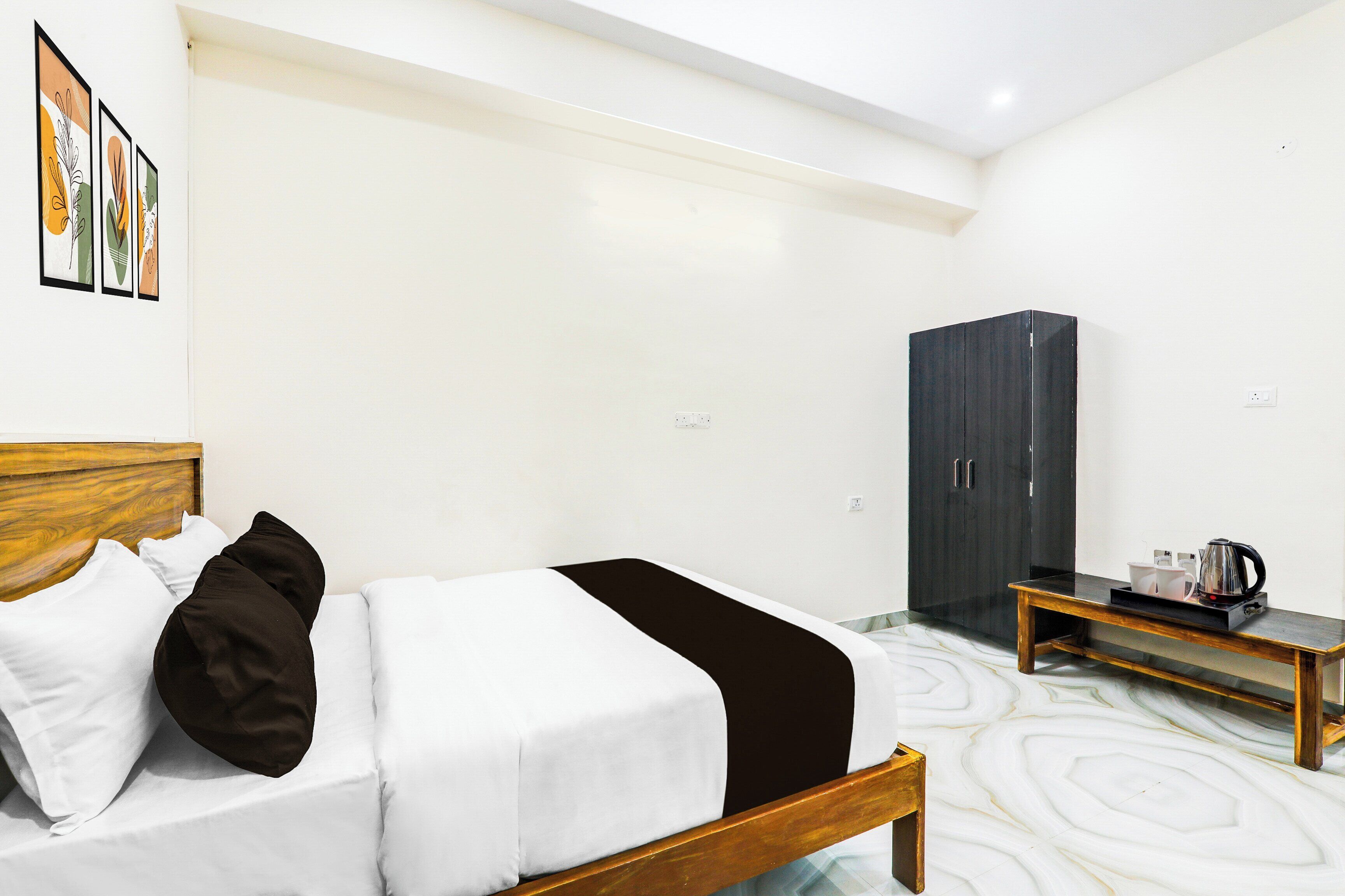 A hotel room with a bed, a wardrobe, a bedside table with a kettle, and a tray with cups.