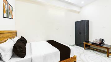 A hotel room with a bed, a wardrobe, a bedside table with a kettle, and a tray with cups.