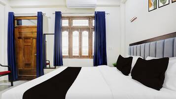 A hotel room with a bed, a window with curtains, a door, and an air conditioning unit.