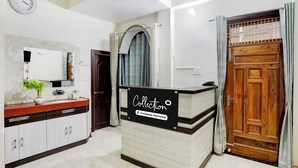 A reception area with a counter, a mirror, a clock, and a wooden door. - Super Collection O Nagwa Lanka Varanasi (Varanasi)