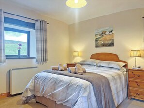 A bedroom with a bed, two bedside lamps, a radiator, a window with curtains, and a painting on the wall. - 2 steps to entrance. (Settle)
