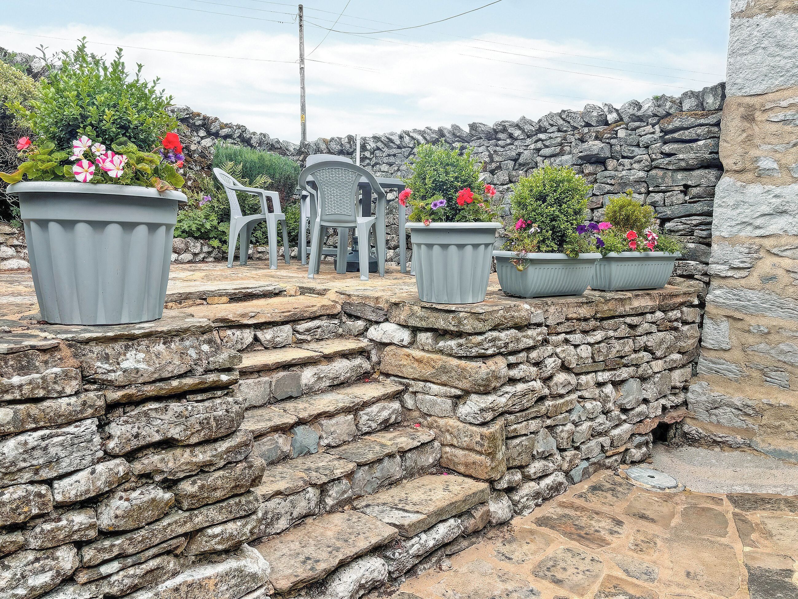 A stone staircase leading to a seating area with potted plants and plastic chairs.