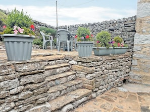 A stone staircase leading to a seating area with potted plants and plastic chairs. - 2 steps to entrance. (Settle)