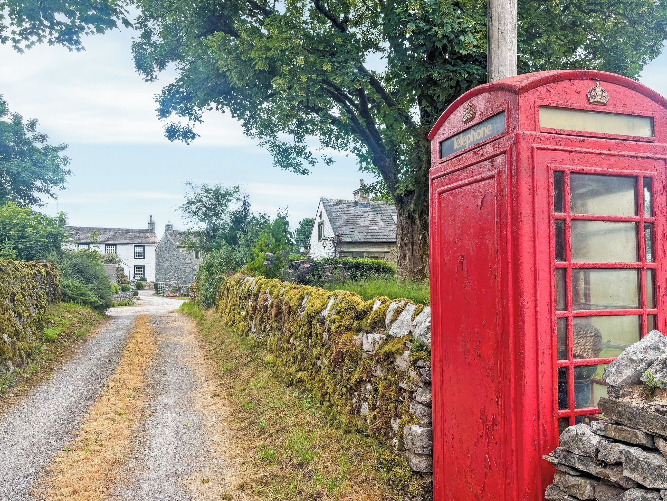 A rural road with a red telephone booth and stone walls.