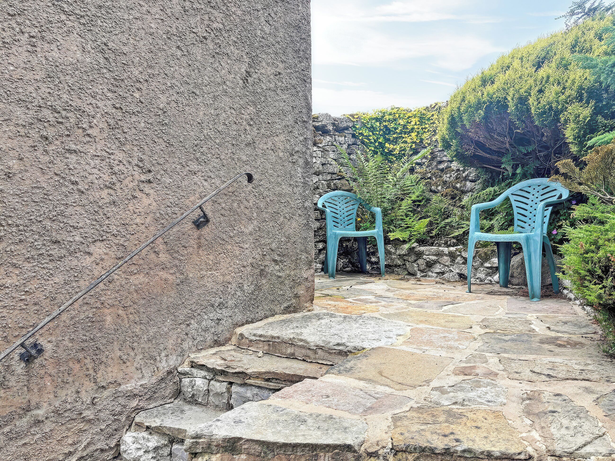 A stone staircase leading to a seating area with two blue plastic chairs.