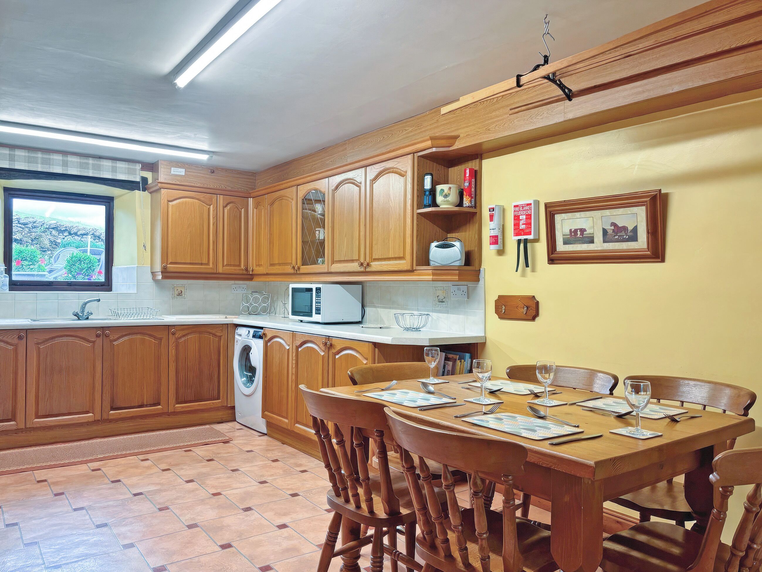 A kitchen with wooden cabinets, a microwave, a washing machine, and a dining area with a table set for four.