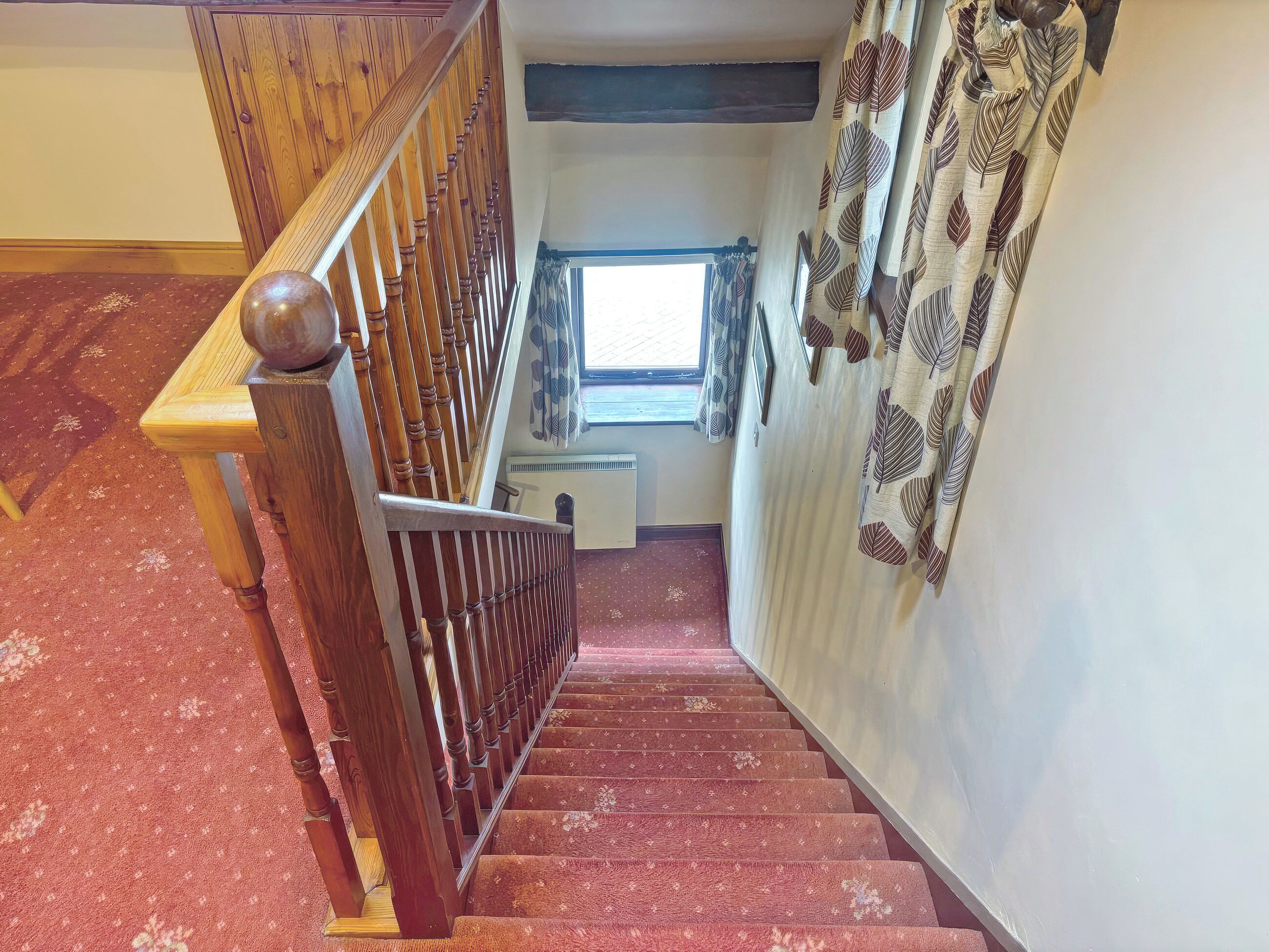 A wooden staircase with a handrail leading to a landing with a window and a radiator.