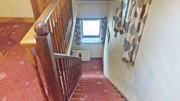A wooden staircase with a handrail leading to a landing with a window and a radiator.