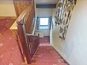 A wooden staircase with a handrail leading to a landing with a window and a radiator.