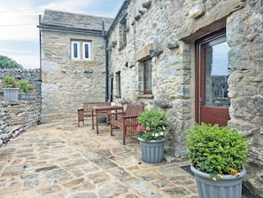 A stone building with a wooden table and chairs, potted plants, and a stone wall. - 2 steps to entrance. (Settle)