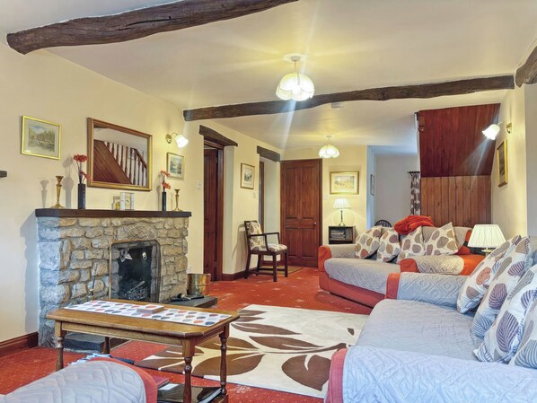 A cozy living room with a stone fireplace, a wooden ceiling beam, and a comfortable seating area with a patterned rug.