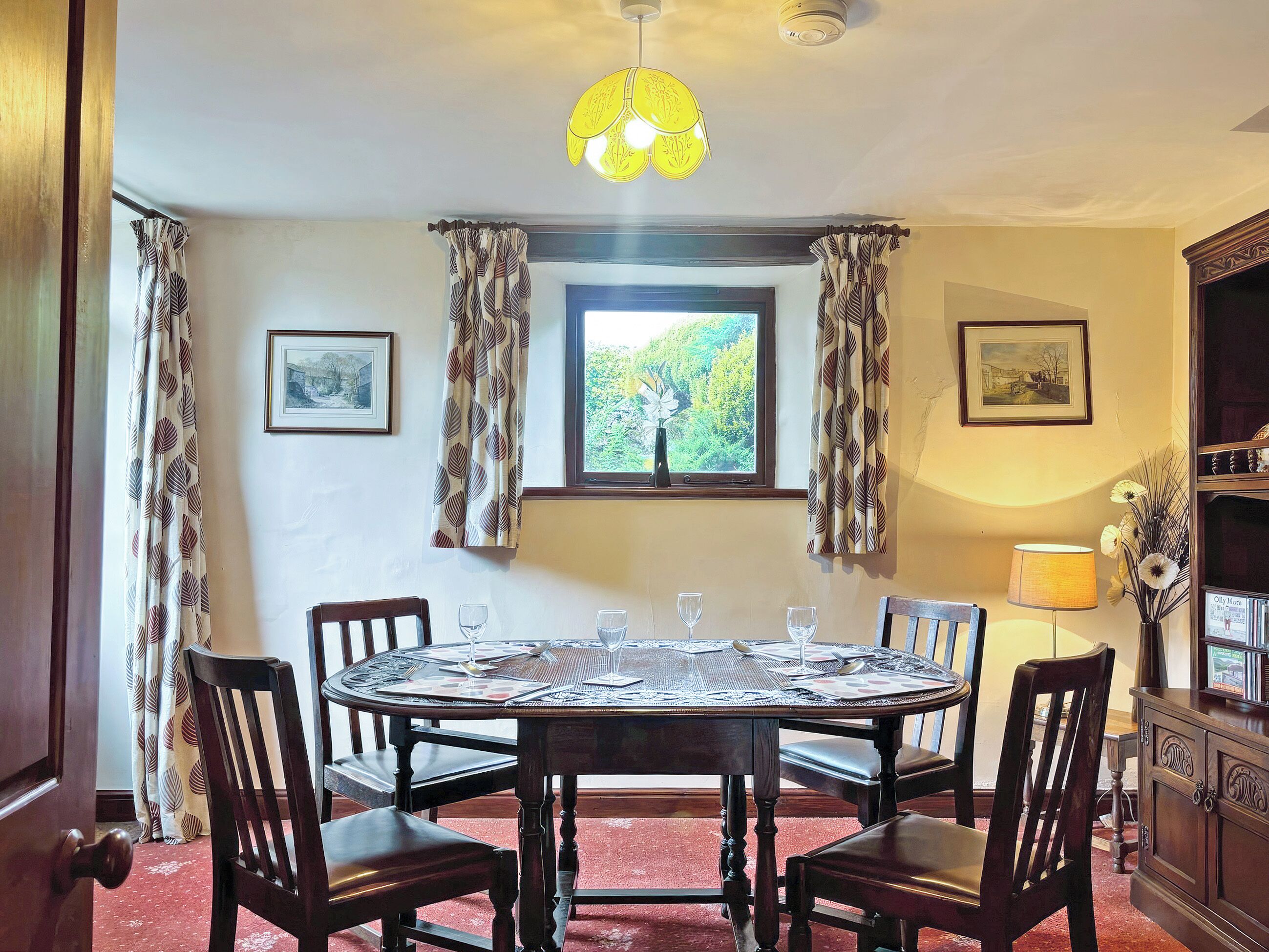 A dining room with a round table, six chairs, a chandelier, a window with curtains, and a cabinet with a mirror.