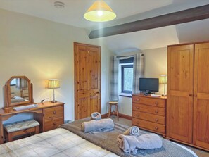 Ein Schlafzimmer mit einem Bett, einem Holzschrank, einem Schreibtisch mit Spiegel, einem Fernseher und einem Fenster mit Vorhängen.