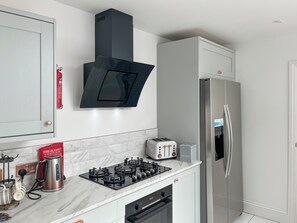 A modern kitchen with a gas stove, a stainless steel refrigerator, and a black range hood. - White House by the Sea (Withernsea)