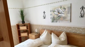 Un dormitorio con cabecera de madera, dos camas, una mesita de noche con lámpara, una planta en maceta y un cuadro floral en la pared.