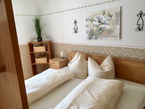 A bedroom with a wooden headboard, two beds, a nightstand with a lamp, a potted plant, and a floral painting on the wall. - Langbürgner See Vacation Apartment, 28 square meters (Rimsting)