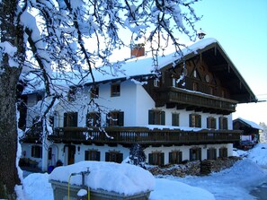 A traditional chalet with a sloped roof, wooden balconies, and a stone foundation. - Langbürgner See Vacation Apartment, 28 square meters (Rimsting)