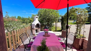 An outdoor patio with a grill, chairs, and a table under a red umbrella. - Langbürgner See Vacation Apartment, 28 square meters (Rimsting)