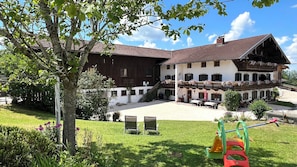 A two-story building with a balcony, a grassy courtyard, and outdoor seating. - Langbürgner See Vacation Apartment, 28 square meters (Rimsting)