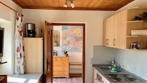 A compact kitchen with wooden cabinets, a coffee maker, and a view into a dining area. - Simssee Vacation Rental, 45 square meters (Rimsting)