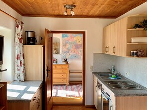 A compact kitchen with wooden cabinets, a coffee maker, and a view into a dining area. - Simssee Vacation Rental, 45 square meters (Rimsting)
