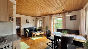 Ein gemütliches Wohnzimmer mit Holzbalkendecke, einem Esstisch mit Stühlen, einer Couch und einer Küchenzeile mit Herd.
