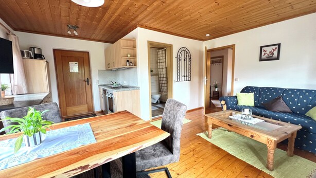 A cozy living area with a wooden dining table, a sofa, and a kitchen in the background. - Simssee Vacation Rental, 45 square meters (Rimsting)