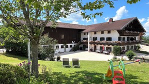 A two-story building with a balcony, a grassy courtyard, and outdoor seating. - Simssee Vacation Rental, 45 square meters (Rimsting)
