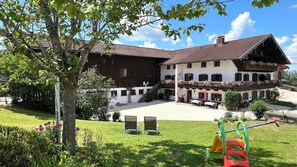 A two-story building with a balcony, a grassy courtyard, and outdoor seating. - Simssee Vacation Rental, 45 square meters (Rimsting)