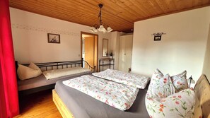 Ein Schlafzimmer mit Holzbalkendecke, einem Bett mit floralem Bettzeug, einem Nachttisch und einem Spiegel.
